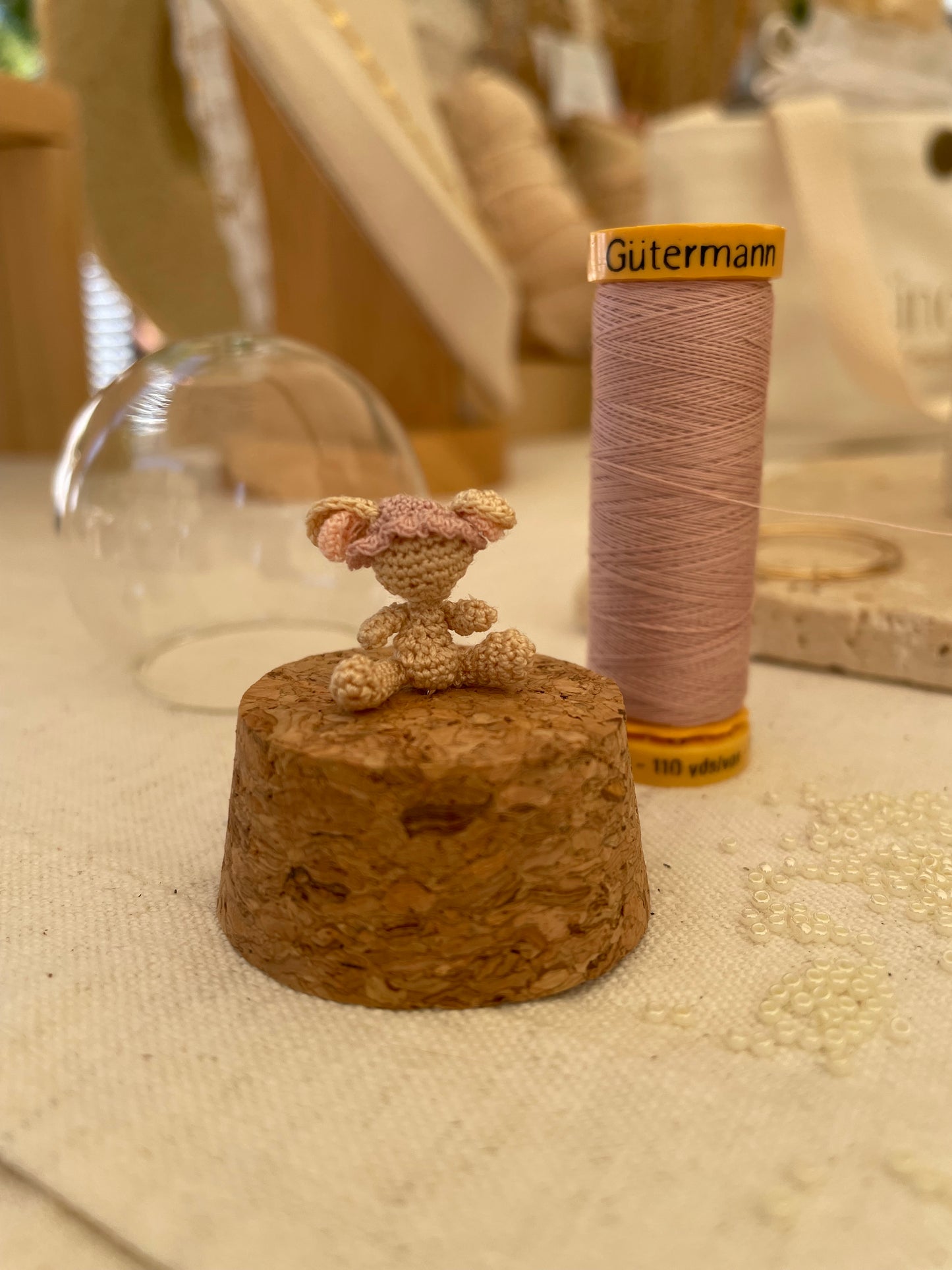 Micro gehaakte muis op kurk van stolp zonder gezicht met Gütermann garenklos erachter.