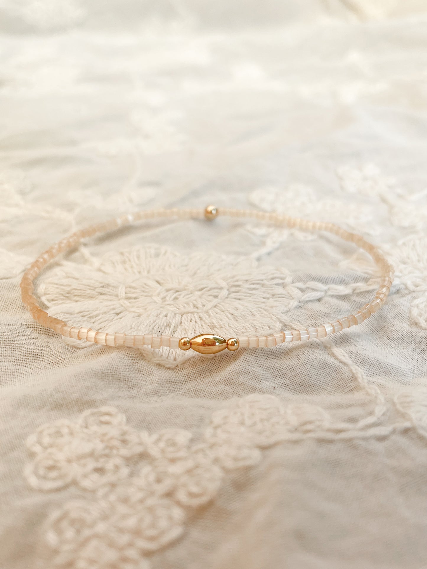 Miyuki beige satijnachtige 2 mm kralen stretch armband, ovalen gold filled kraal tussenstuk 3-5 mm, 2 gold filled kraaltjes naast ovalen.