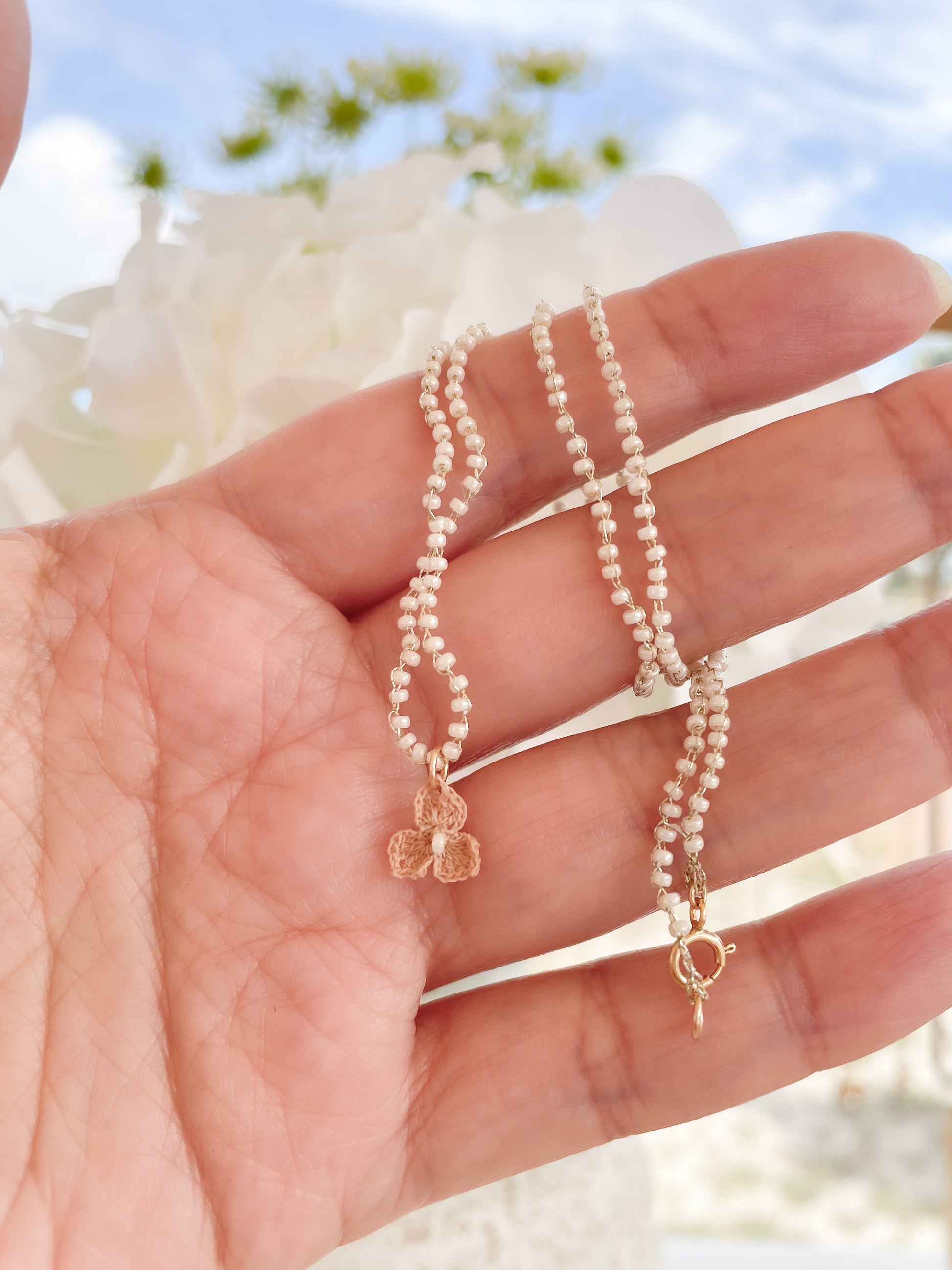 Aiyana ketting Sfeerfoto; gehaakte ketting en bedel, ambacht, vlinder bedel gehaakt donkerbeige, ketting gehaakt van gouddraad en witte Miyuki kraaltjes 