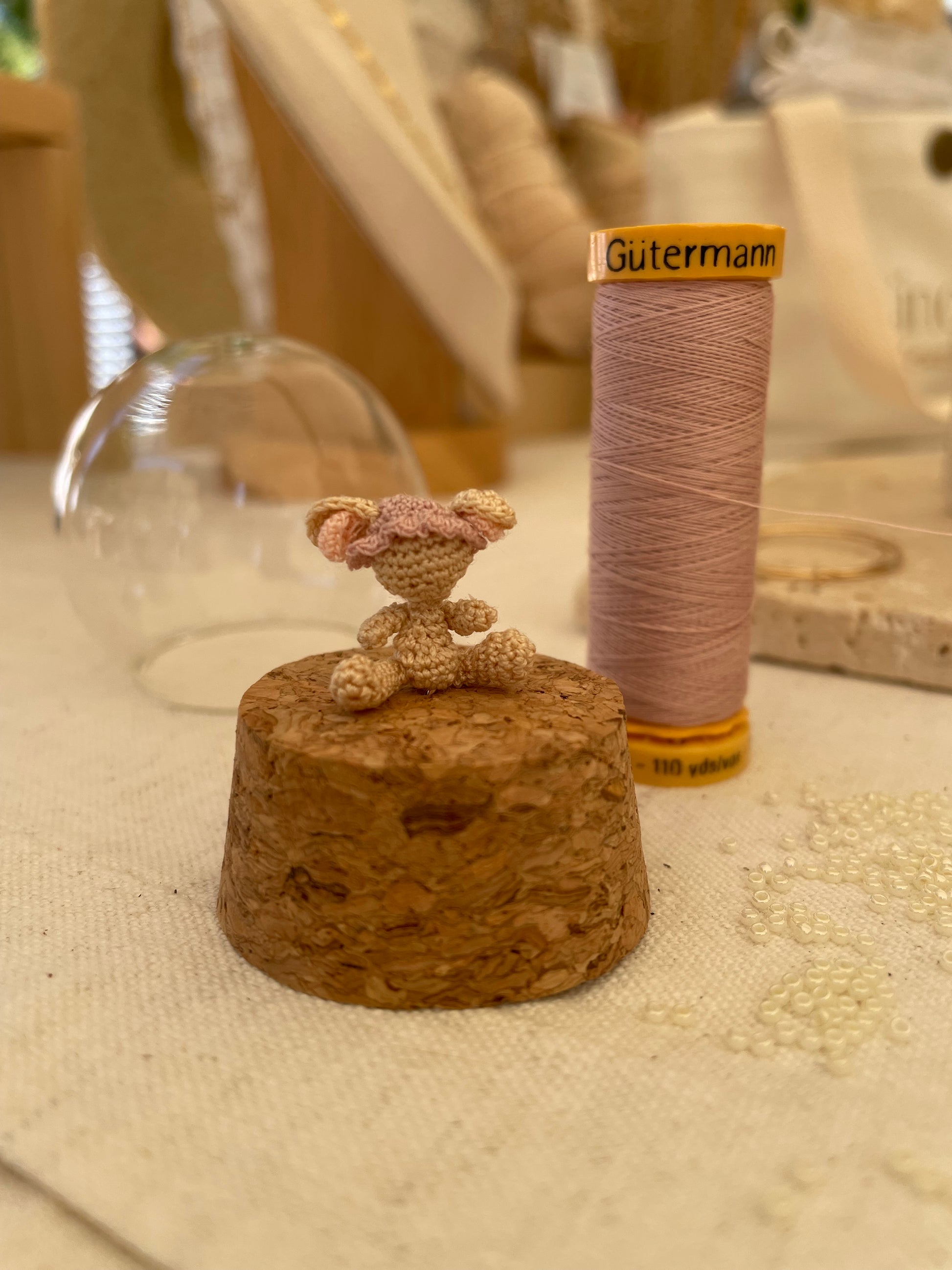 Micro gehaakte muis op kurk van stolp zonder gezicht met Gütermann garenklos erachter. 