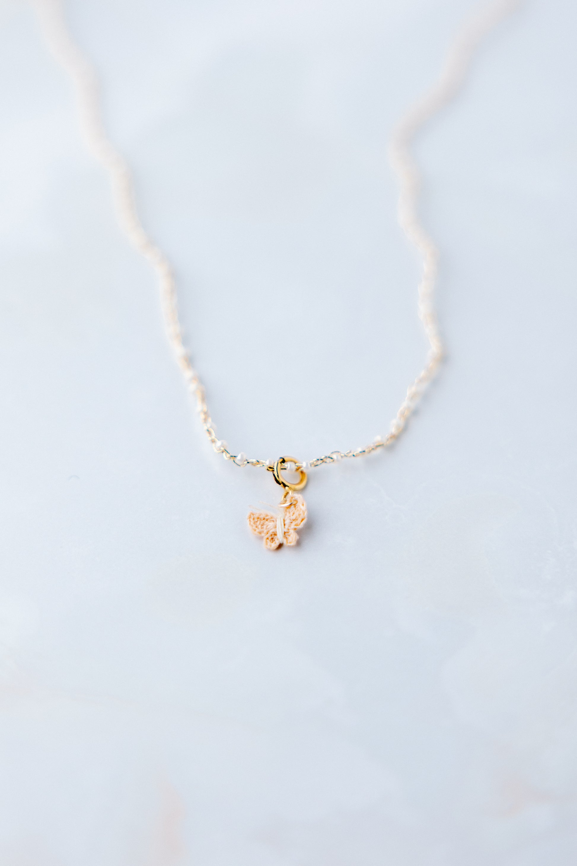Sfeer foto Yara micro gehaakte vlinder ketting; ambacht, vlinder gehaakt van naaigaren donkerbeige, ketting gehaakt met gouddraad en 1 mm glaskraaltjes